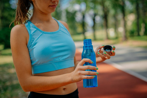 Милая спортивная девушка собирается выпить воды после того, как она открыла бутылку - Фото, изображение