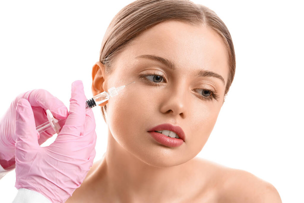 Genç bir kadın, beyaz arka planda yüzüne enjeksiyon yaptırıyor. - Fotoğraf, Görsel