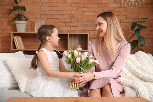Милая маленькая девочка приветствует свою мать тюльпанами дома - Фото, изображение