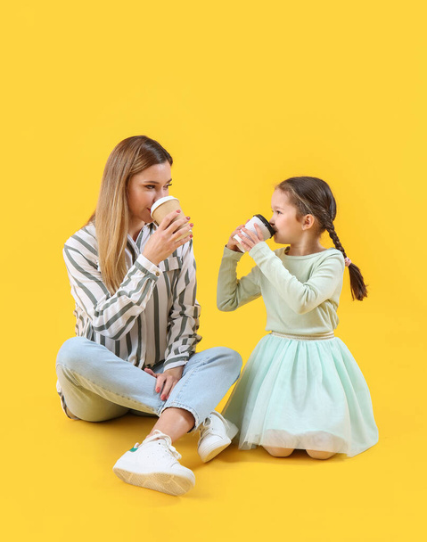 Menina bonito com sua mãe bebendo café no fundo amarelo - Foto, Imagem