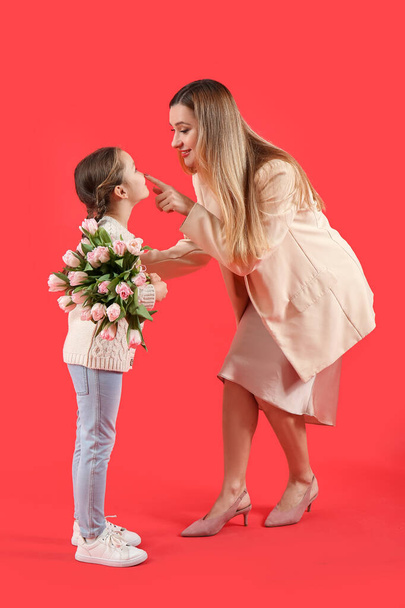 Anya megérinti a kislánya orrát tulipánnal a piros háttér - Fotó, kép