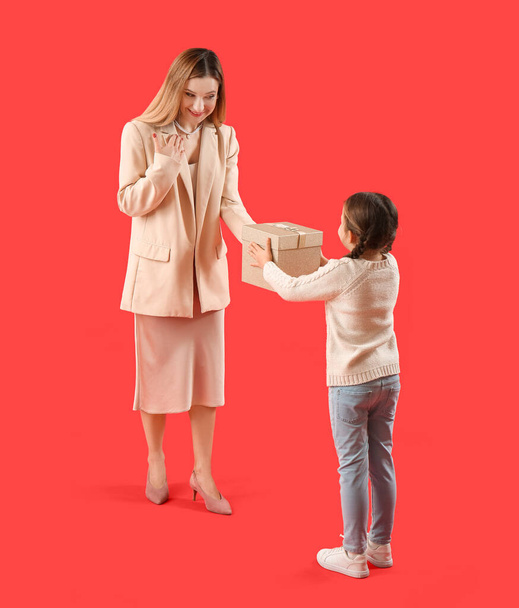 Cute little girl greeting her mother with gift on red background - Photo, Image