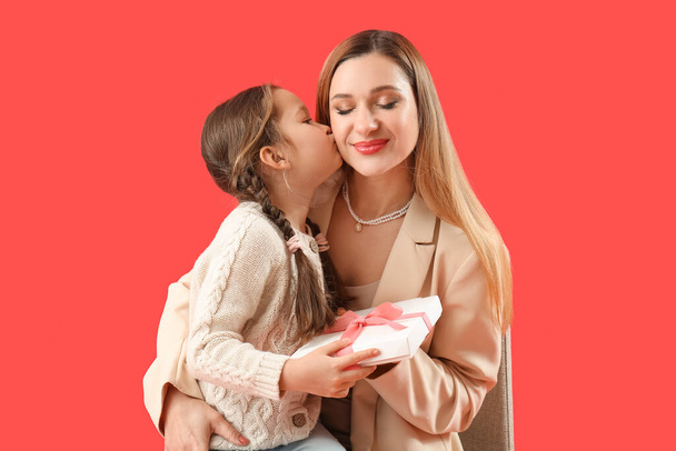 Cute little girl with her mother and gift on red background - Foto, afbeelding