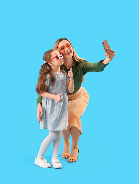 Милая маленькая девочка со своей матерью, делающей селфи на синем фоне - Фото, изображение