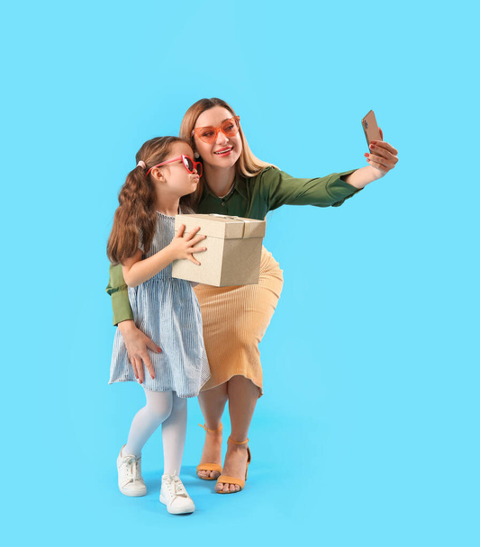 Χαριτωμένο κοριτσάκι με τη μητέρα της και δώρο τη λήψη selfie σε μπλε φόντο - Φωτογραφία, εικόνα