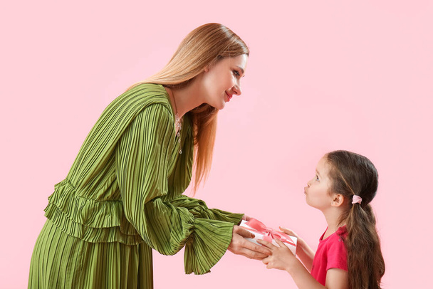 Linda niña saludando a su madre con regalo sobre fondo rosa - Foto, Imagen