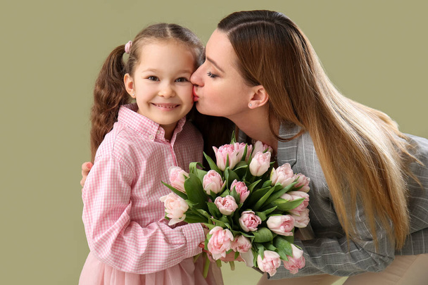 Mother kissing her little daughter with tulips on green background - Foto, afbeelding
