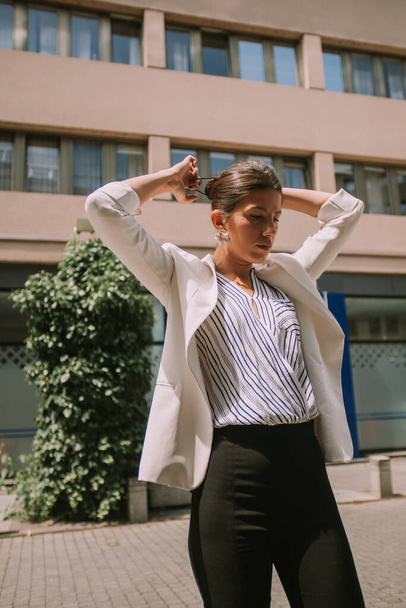 Beautiful business woman fixing her bun while standing near the building - Фото, изображение