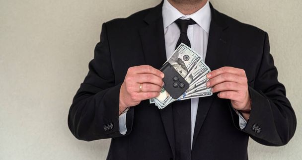 business man in a serious suit stands in the hallway of the office with a large sum of dollars in his hands. Concept of rich man from the office - 写真・画像