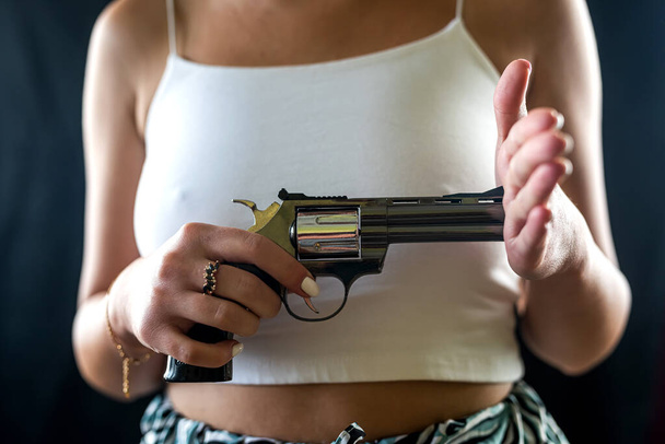 komoly nő, elegáns ruhákban, arctalan, fekete háttérrel elszigetelt revolver fegyverrel. Lövöldözés fegyverrel. egy nő gyilkos fegyverrel. - Fotó, kép