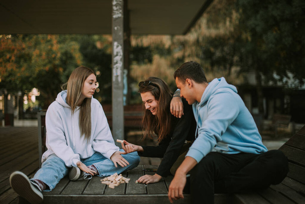 Drei Freunde unterhalten sich auf der Holzbank über das verstreute Jenga - Foto, Bild