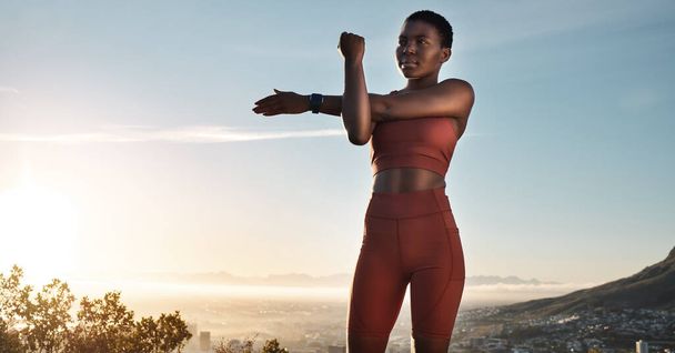 Fitness, black woman and stretching arm on mountains, blue sky or sunset for wellness, healthy goals or energy. Focus, athlete and sports warm up, exercise and start body training with strong mindset. - Fotó, kép