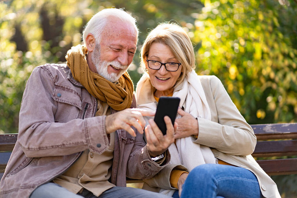 ηλικιωμένο ζευγάρι που χρησιμοποιεί τηλέφωνο στο πάρκο  - Φωτογραφία, εικόνα