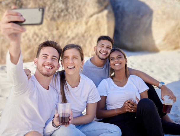Friends, selfie and beach for a picnic, drinks and happiness with couple on double date and online for social media update. Diversity men and women with phone on ocean sand for fun, love and bonding. - Foto, imagen