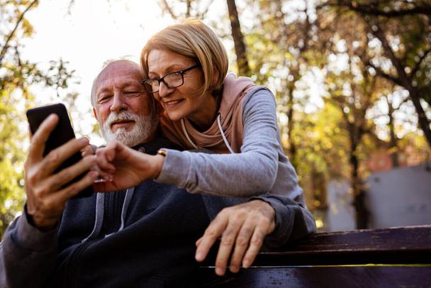 ηλικιωμένο ζευγάρι που χρησιμοποιεί τηλέφωνο στο πάρκο  - Φωτογραφία, εικόνα