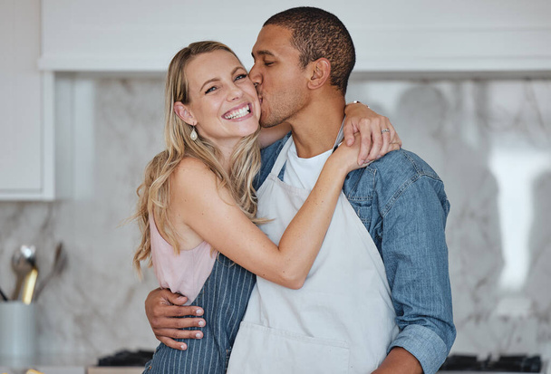 Love, interracial and couple kiss in kitchen, happiness and loving together for relationship. Romance, man and woman with embrace, kissing and celebrate for anniversary, cooking and relax with hug - Photo, Image