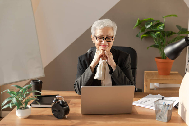 Magabiztos, stílusos, középkorú európai nő, aki laptopot használ a munkahelyén. Stílusos idősebb érett 60-as évekbeli ősz hajú nő üzletasszony ül irodai asztalnál. Vezető tanár szakmunkás - Fotó, kép