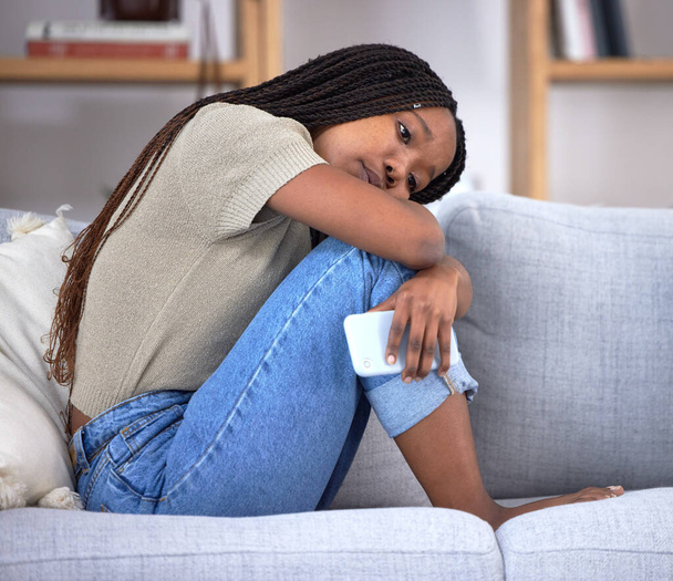 Breakup depression, sad and thinking black woman with a phone after communication, problem and anxiety about email on the couch. Mental health, idea and African girl depressed about chat fail. - 写真・画像