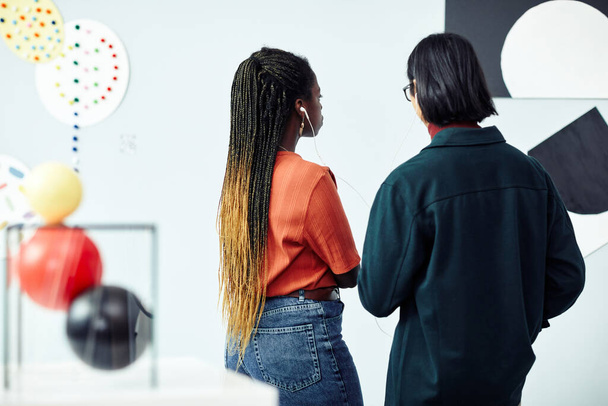 Zadní pohled na etnicky různorodého mladíka a ženu při pohledu na abstraktní malbu a poslechu audio turné na výstavě v galerii umění - Fotografie, Obrázek