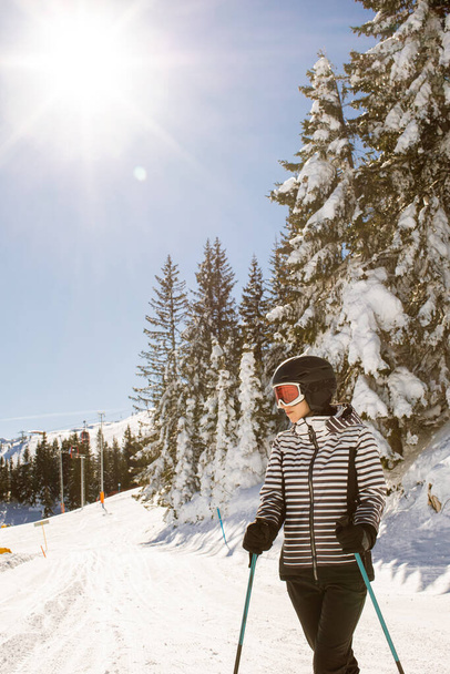 Jeune femme profitant de la journée hivernale de ski sur les pistes enneigées, entourée de grands arbres et habillée pour le froid - Photo, image