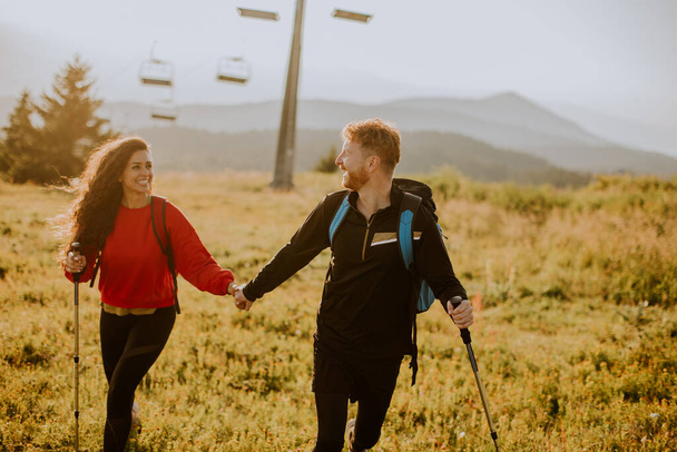 Uśmiechnięta młoda para spacerująca z plecakami po zielonych wzgórzach - Zdjęcie, obraz