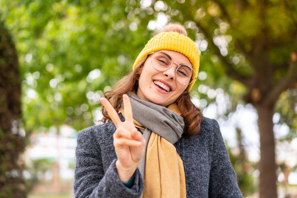 Brunette woman wearing winter jacket at outdoors smiling and showing victory sign - Foto, immagini