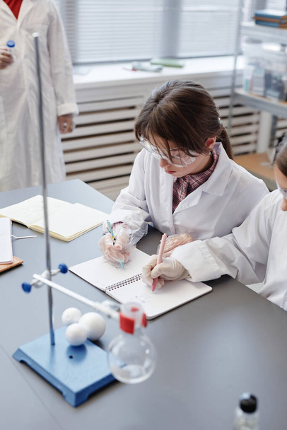 Retrato vertical de crianças tomando notas enquanto fazem experimentos científicos no laboratório de química da escola - Foto, Imagem