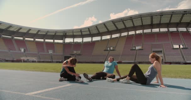 Deportistas relajándose y estirándose mientras están sentados en una pista deportiva - Metraje, vídeo