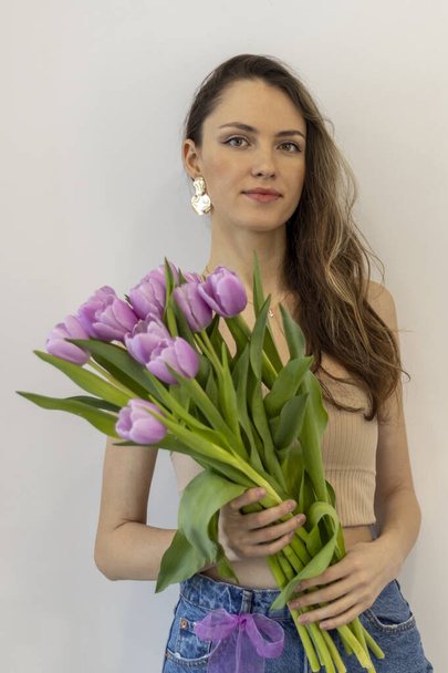 Hermosa joven mujer de moda con un ramo de tulipanes sobre un fondo beige. Primer plano. - Foto, imagen