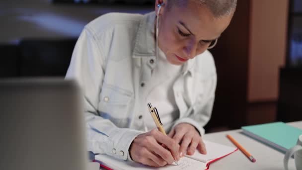 Mujer adulta escribiendo notas viendo curso de video en línea en casa acogedora por la noche - Imágenes, Vídeo