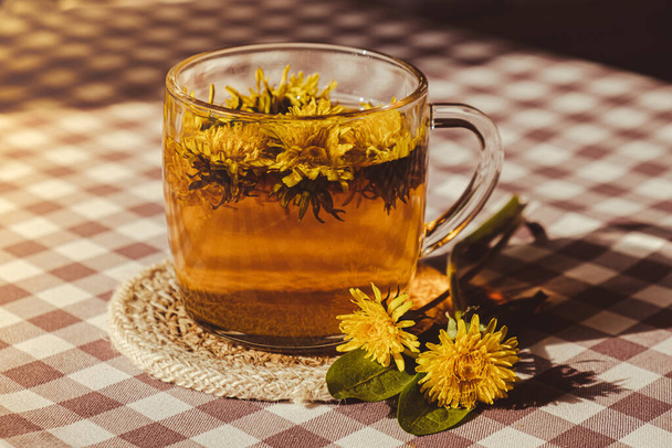 Dandelion flower healthy tea in glass cup on table. Herbal medicine Delicious tisane tea from with fresh yellow blossom dandelion flowers inside tea cup. Green clearing infusion Wildflowers Eco - Foto, Imagen