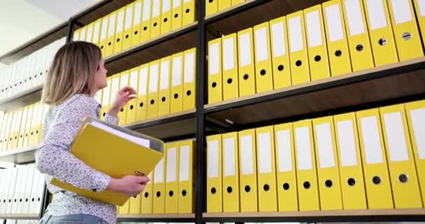Žena sekretářka vytahuje žlutou složku z horní police knihovny v kanceláři 4k film zpomalení. Byrokracie v podnikatelské koncepci - Záběry, video