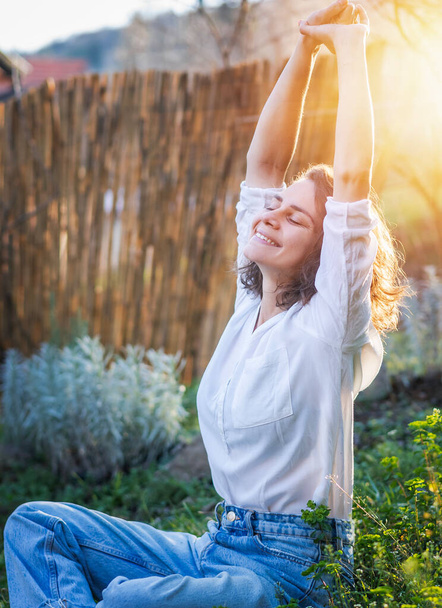 Young caucasian pretty woman in white shirt enjoying spring summer sun sitting on green grass - Fotografie, Obrázek