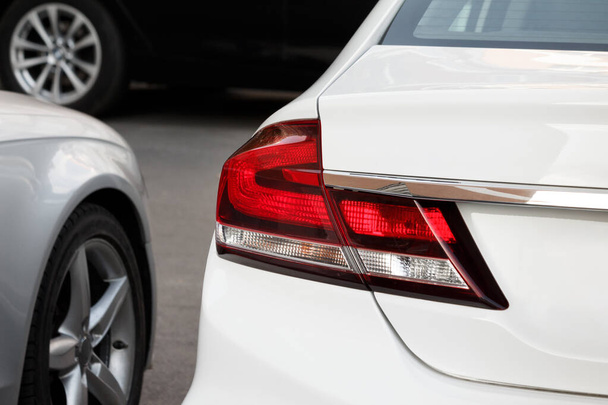Modern white car parked on asphalt. Close-up back view with headlight, bumper and car wheels blured at background - 写真・画像