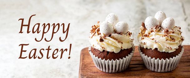Holiday card. Happy Easter. Chocolate cupcakes, sweet candy eggs and cream cheese nest. Homemade cake dessert. - 写真・画像