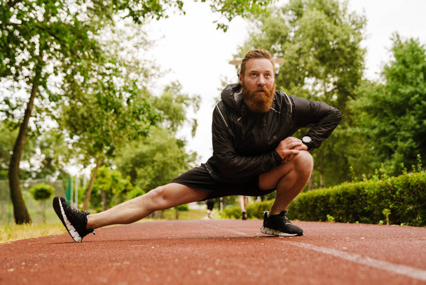 Ginger bearded sportsman doing exercise while working out in park outdoors - Zdjęcie, obraz