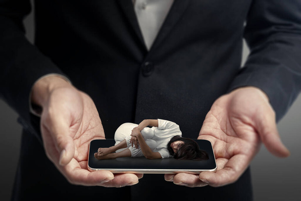 Businessman hand holding mobile phone screen with a view of depressed woman sitting. Cyberbullying Concept - Fotografie, Obrázek
