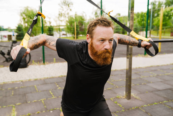 Ginger bearded sportsman doing exercise while working out on playground outdoors - Fotoğraf, Görsel
