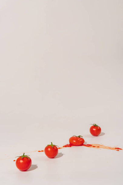 Fresh cherry tomatoes in a line on a light background. One is smashed. Minimal natural food concept with copy space - Фото, зображення