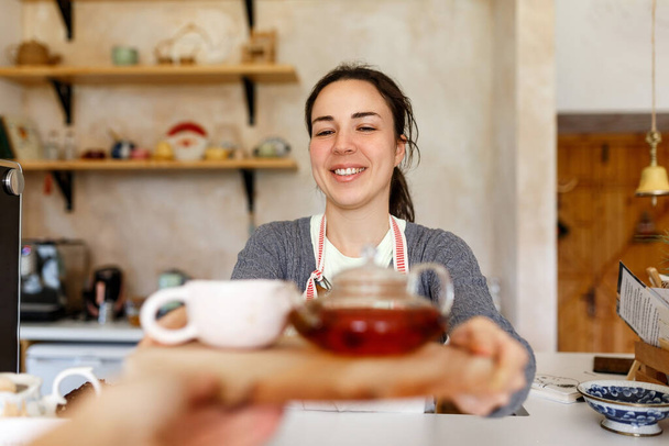 Happy young woman in apron, startup come true. Small business concept. Family business, cafe place. Giving orders, holding tea tray and cup, close up. - Φωτογραφία, εικόνα