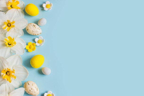 ¡Feliz Pascua! Huevos de Pascua y narcisos amarillos flores planas ponen sobre fondo azul. Plantilla festiva con estilo con espacio para texto. Tarjeta de felicitación o banner - Foto, imagen