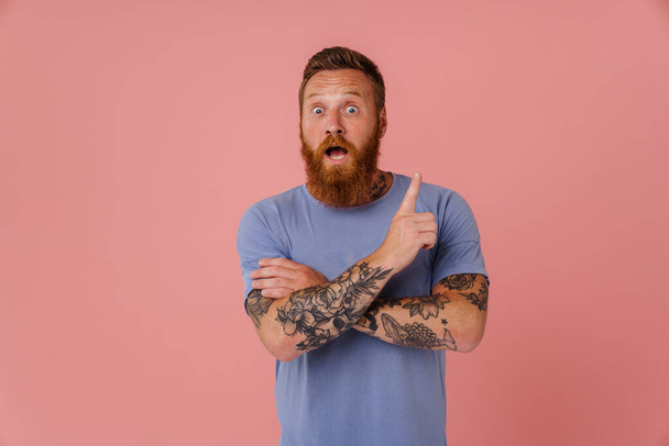 Ginger shocked man with beard pointing finger upward isolated over pink background - Фото, зображення