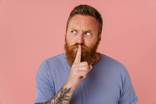 Ginger white man with tattoo frowning and showing silence gesture isolated over pink background - Фото, зображення