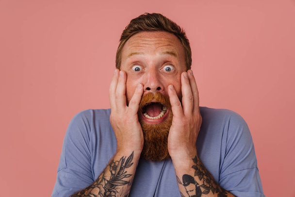 Ginger scared man with beard expressing surprise at camera isolated over pink background - Photo, Image
