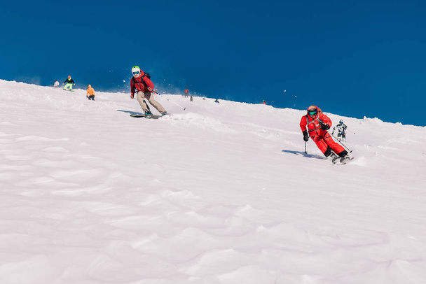 Karpaty, Ukraine, February 8, 2023. Skiers and snowboarders freeride in clear sunny weather on the slopes of the mountains near the resort of Dragobrat. High quality photo - Fotoğraf, Görsel