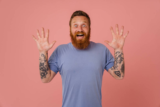Ginger shocked man with beard expressing surprise at camera isolated over pink background - Foto, Bild