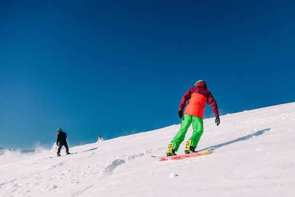 Karpaty, Ukraine, February 8, 2023. Skiers and snowboarders freeride in clear sunny weather on the slopes of the mountains near the resort of Dragobrat. High quality photo - Фото, изображение