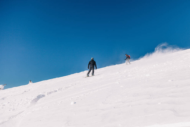 Karpaty, Ukraine, February 8, 2023. Skiers and snowboarders freeride in clear sunny weather on the slopes of the mountains near the resort of Dragobrat. High quality photo - Fotografie, Obrázek