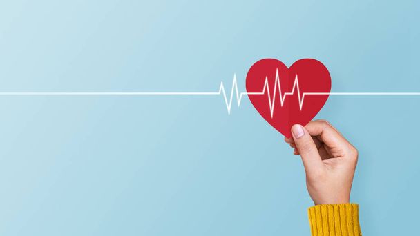 Frau hält rotes Papierherz mit Kardiogramm auf blauem Hintergrund. Konzept von Valentinstag, Liebe, Gesundheitsfürsorge - Foto, Bild