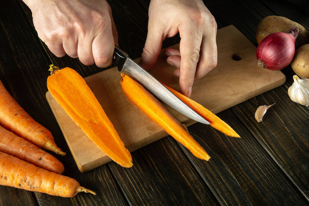 Kucharz kroi surowe marchewki na małe kawałki nożem. Zbliżenie rąk szefa kuchni podczas pracy w kuchni. Gotowanie pyszne śniadanie lub kolację - Zdjęcie, obraz
